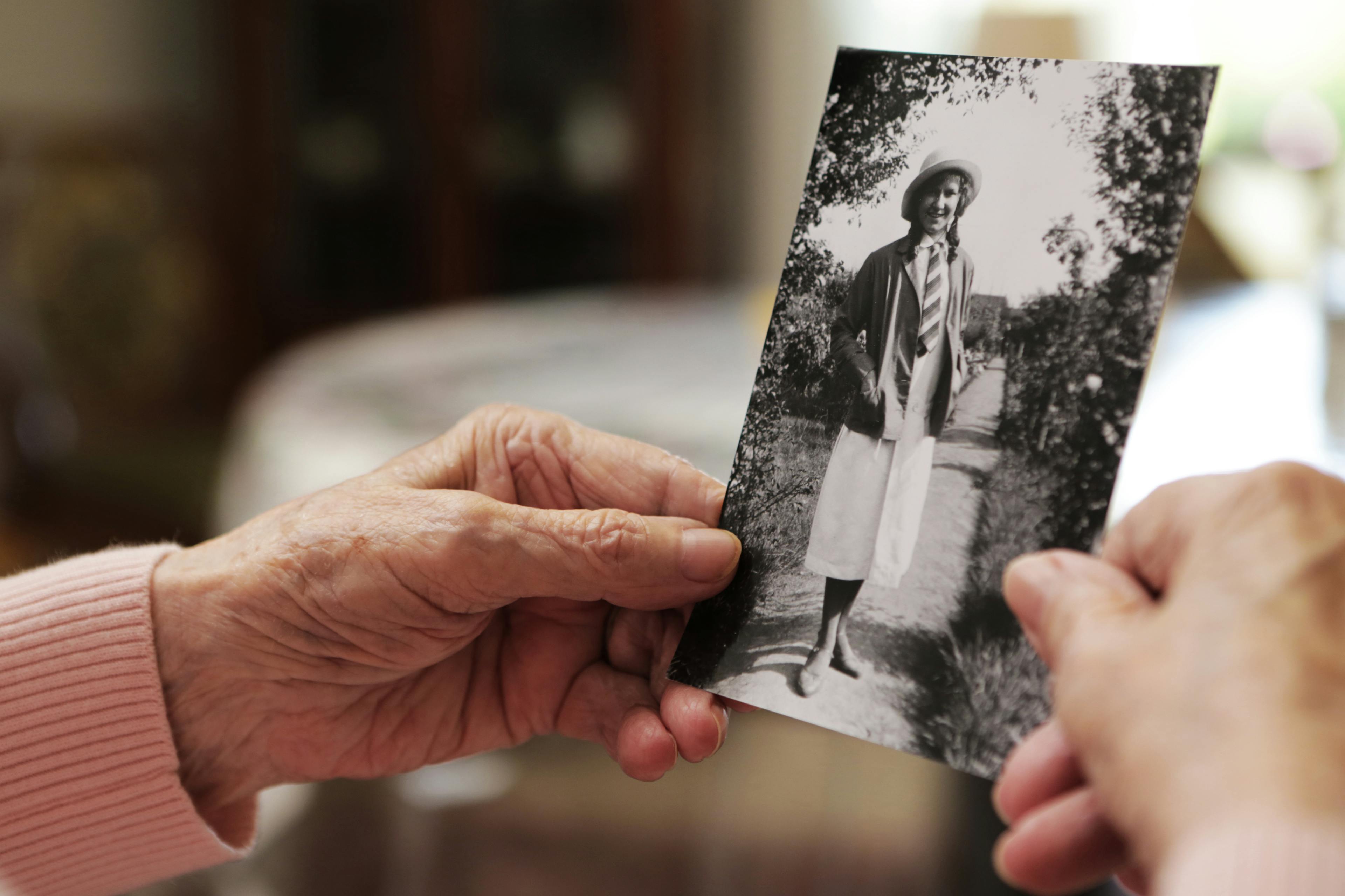 Alternativer Text: Ältere Hände halten ein Schwarz-Weiß-Foto einer lächelnden Person in historischer Kleidung.